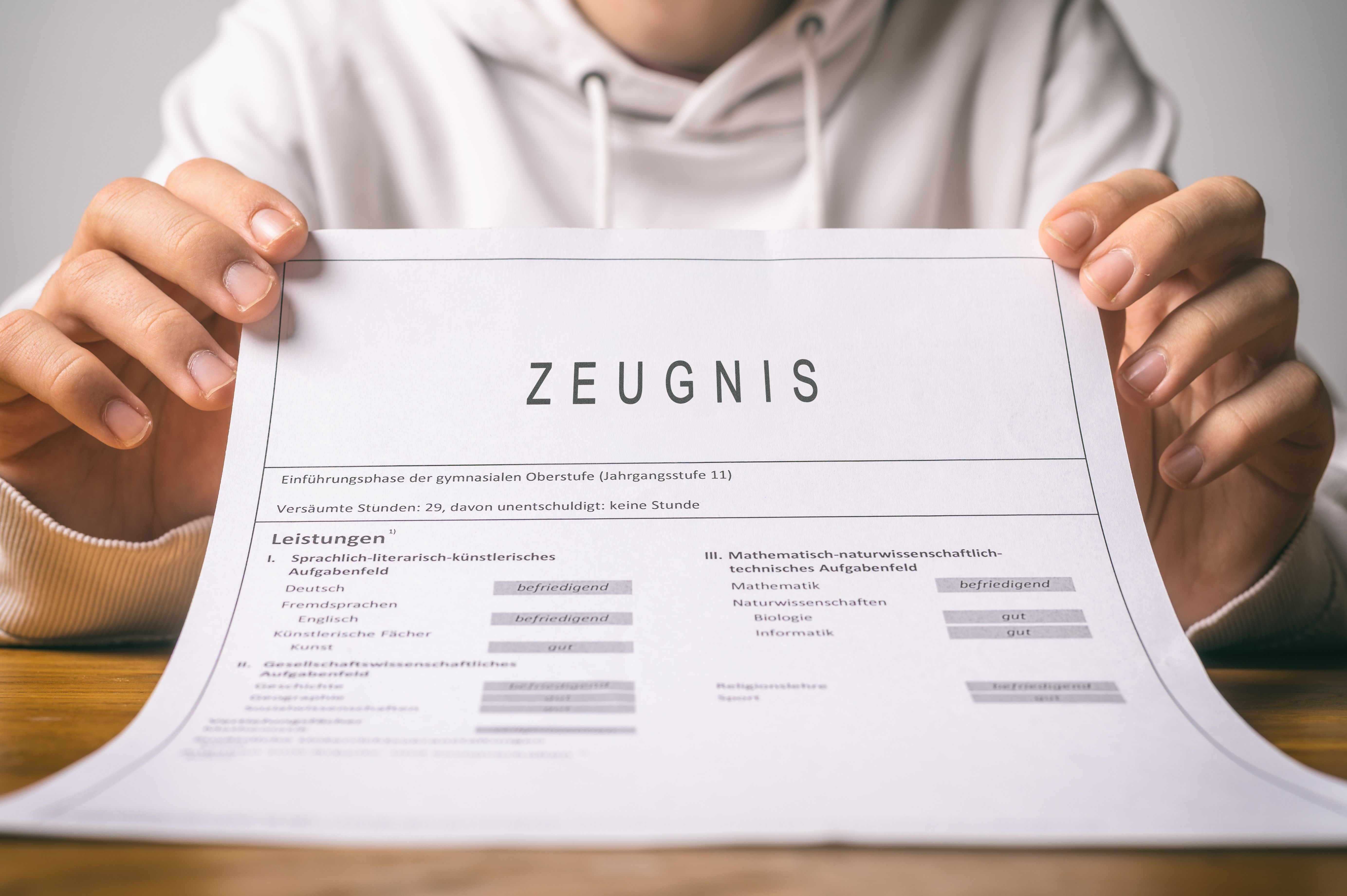 Person präsentiert ein Zeugnis mit dem Schriftzug „Zeugnis“ in der Nahaufnahme