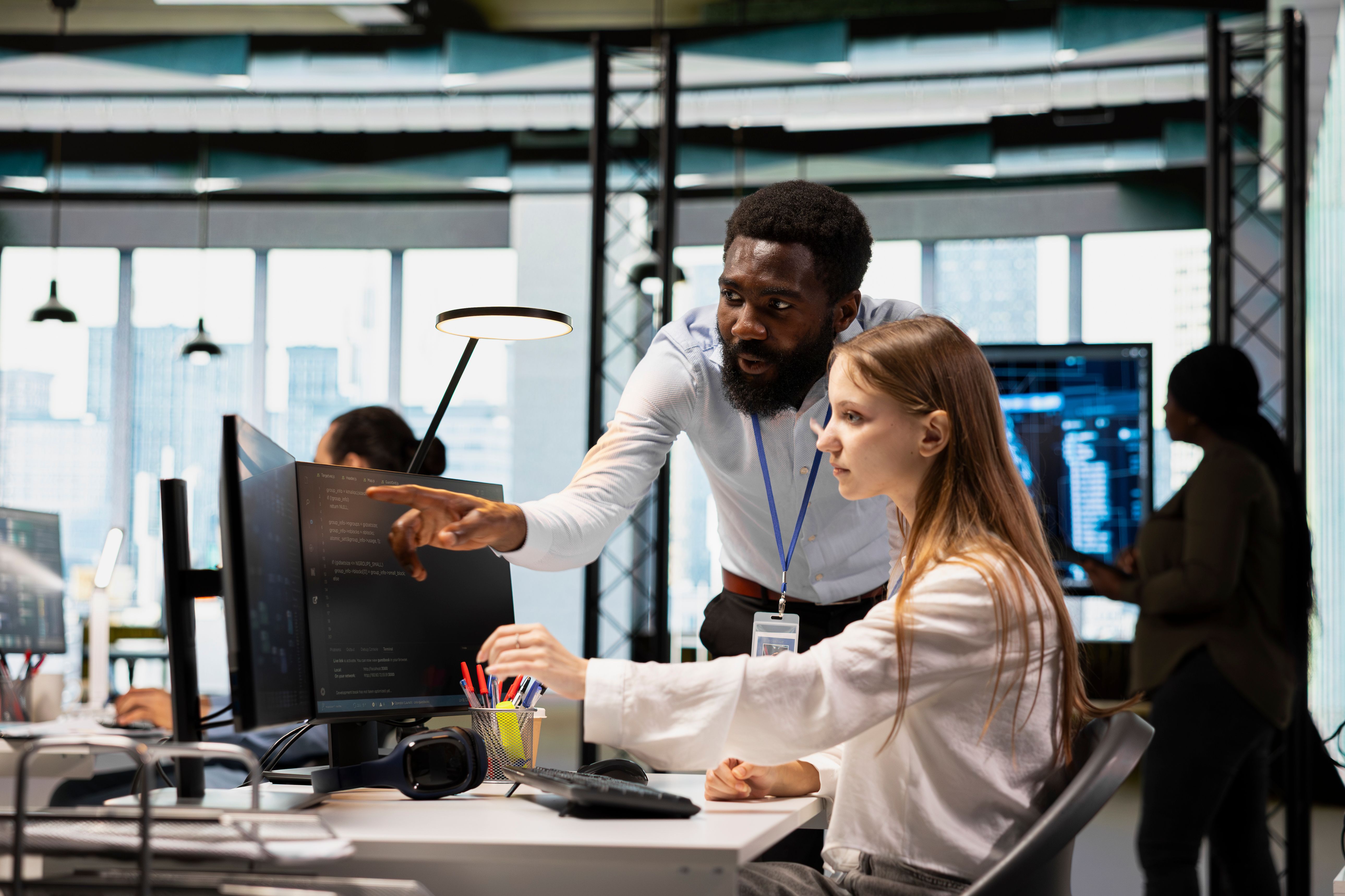 Leitender Programmierer unterstützt neuen Mitarbeiter am PC in einer Softwareentwicklungsagentur. Afroamerikanischer IT-Experte hilft Praktikanten beim Programmieren und Coding während des Internships.