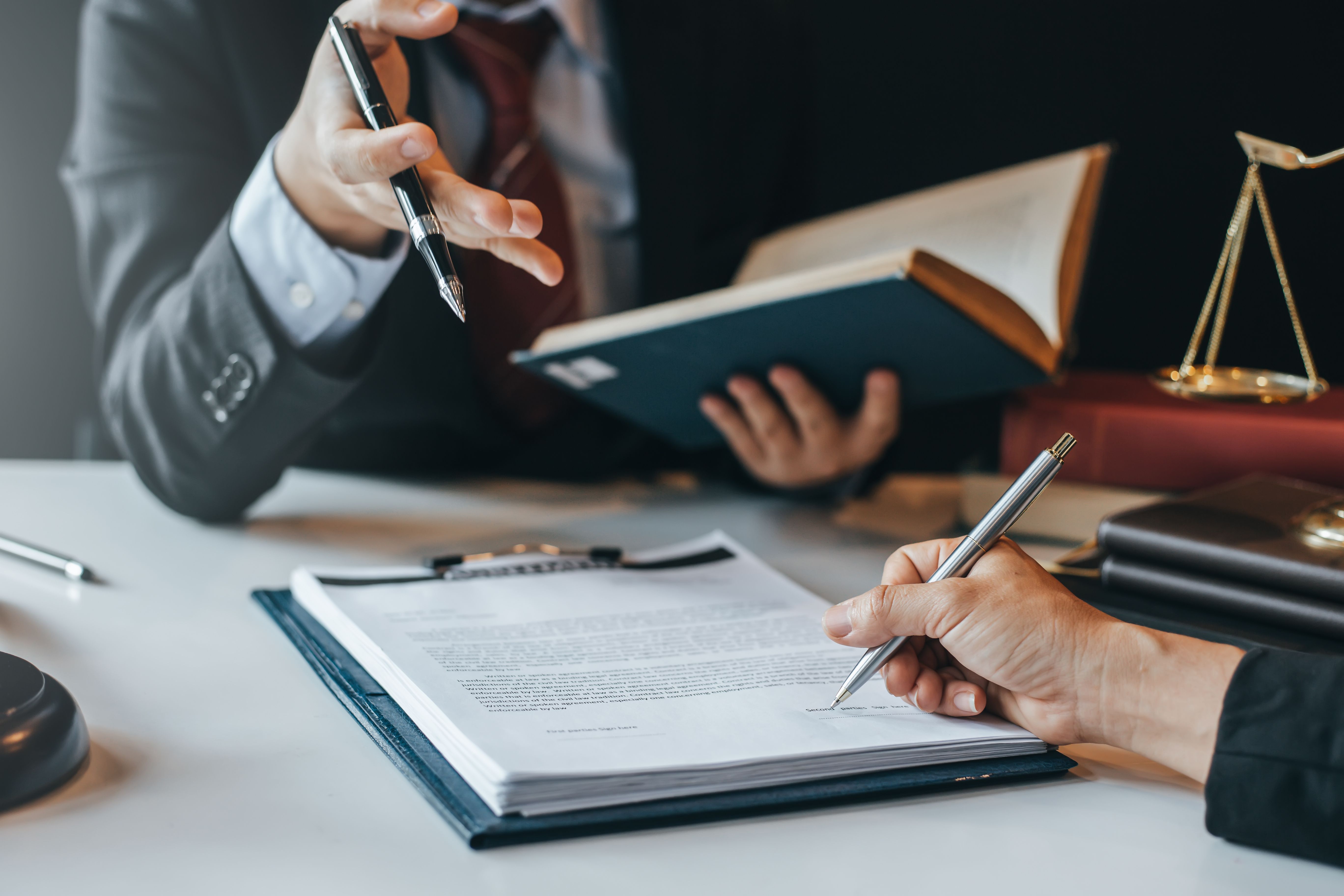 Person unterschreibt einen Arbeitsvertrag im Gespräch mit einem Berater – Symbolbild für die Kündigung oder vorzeitige Beendigung eines befristeten Arbeitsvertrags.