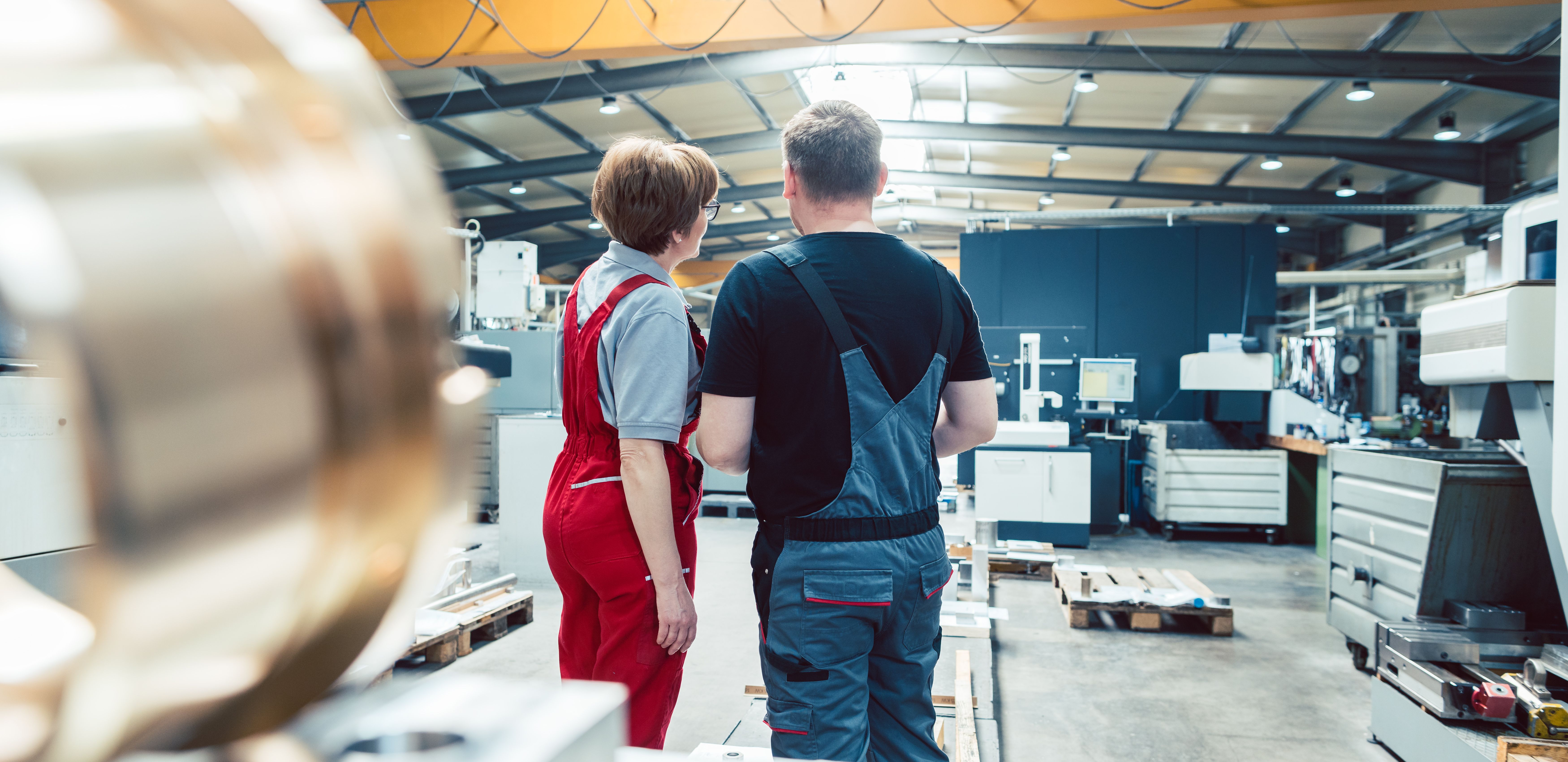 Zwei Fachkräfte in einer modernen Produktionshalle in Thüringen bei der Besichtigung von Industrieanlagen und Maschinen.
