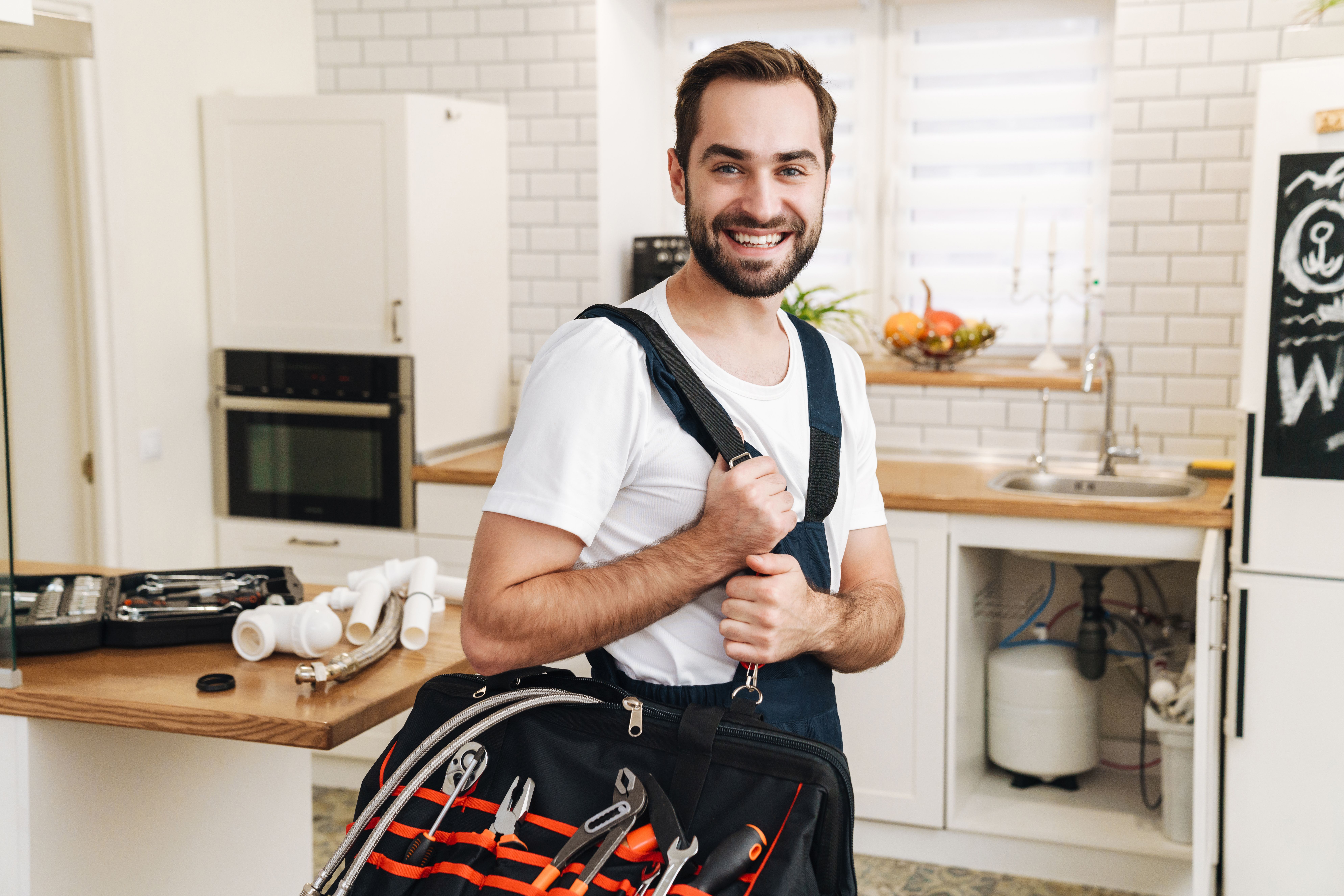 Klempner mit Werkzeugtasche steht in einer Küche und ist bereit für Reparatur- oder Installationsarbeiten.