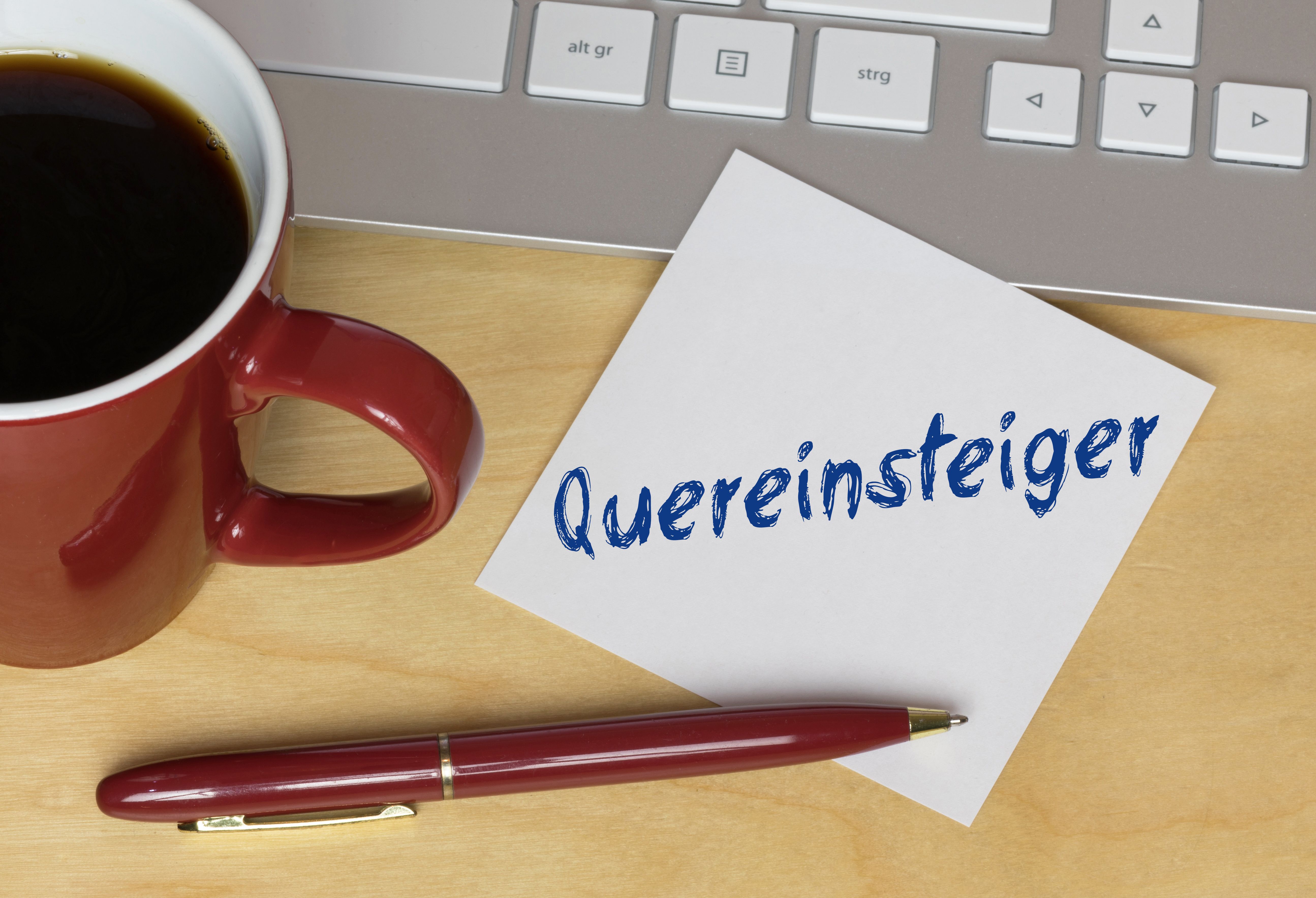 Notizzettel mit der Aufschrift „Quereinsteiger“ neben Kaffeetasse, Tastatur und Stift