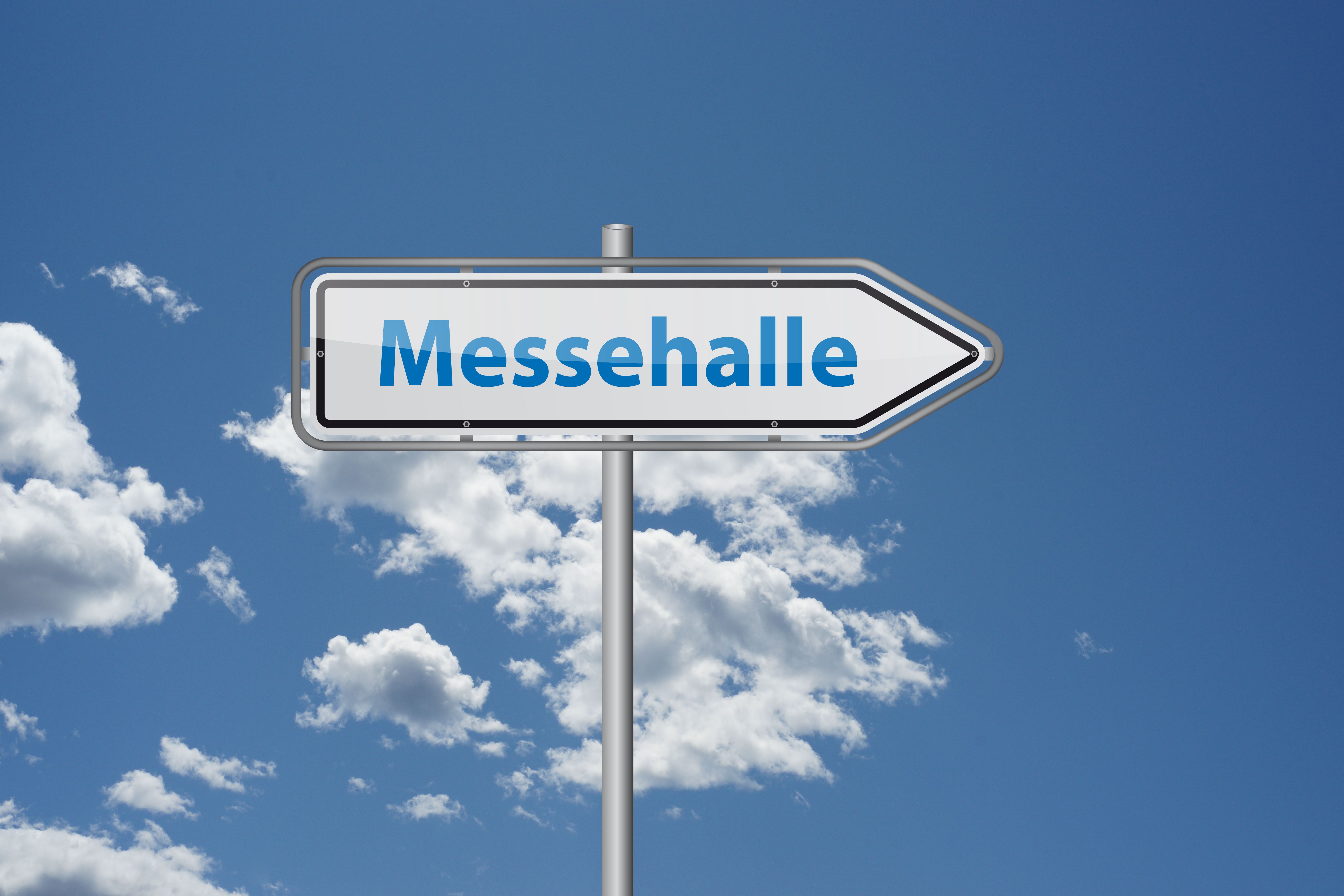 Wegweiser zur Messehalle unter blauem Himmel.
