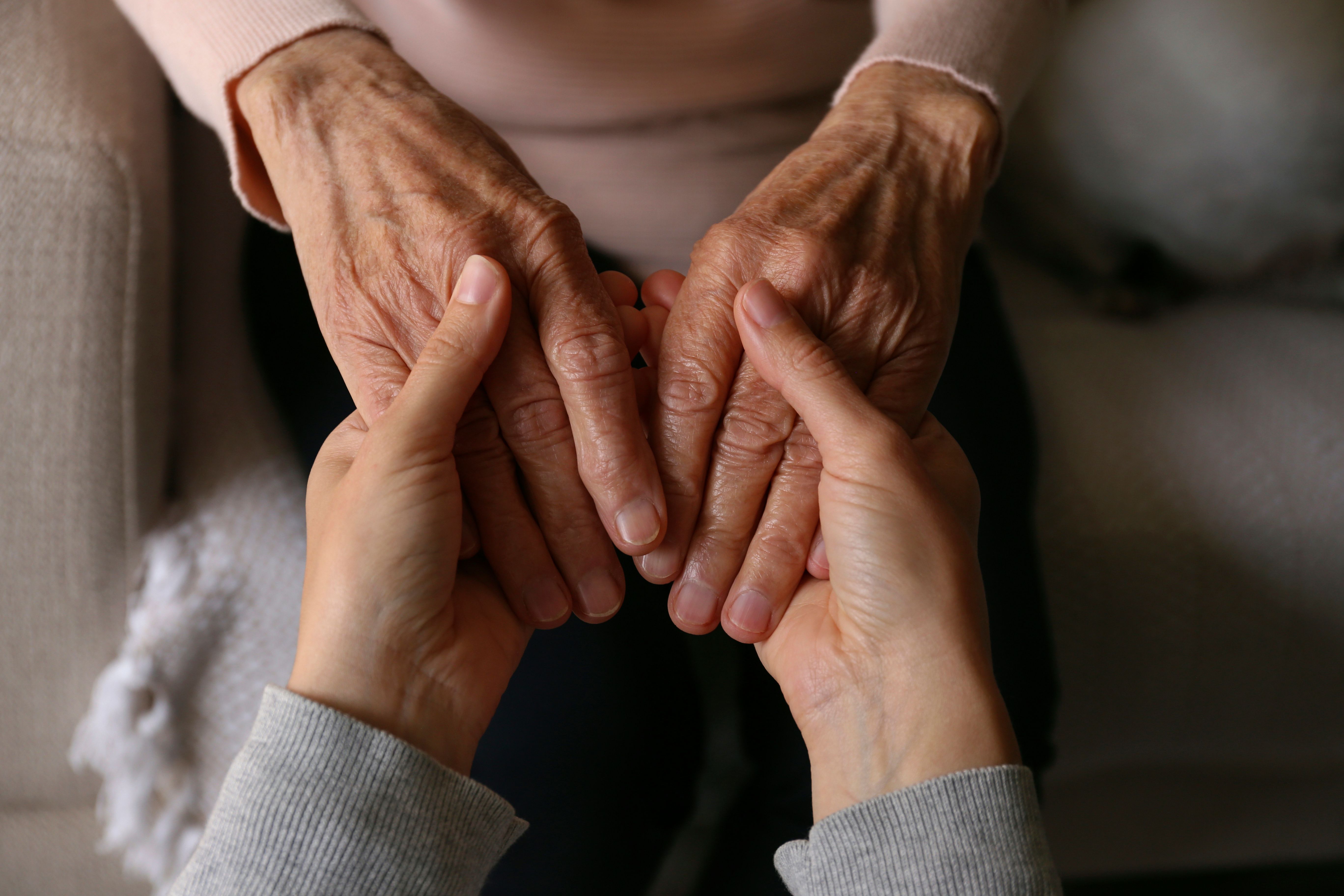 Pflegekraft hält einfühlsam die Hände einer älteren Person als Zeichen von Unterstützung und Betreuung.