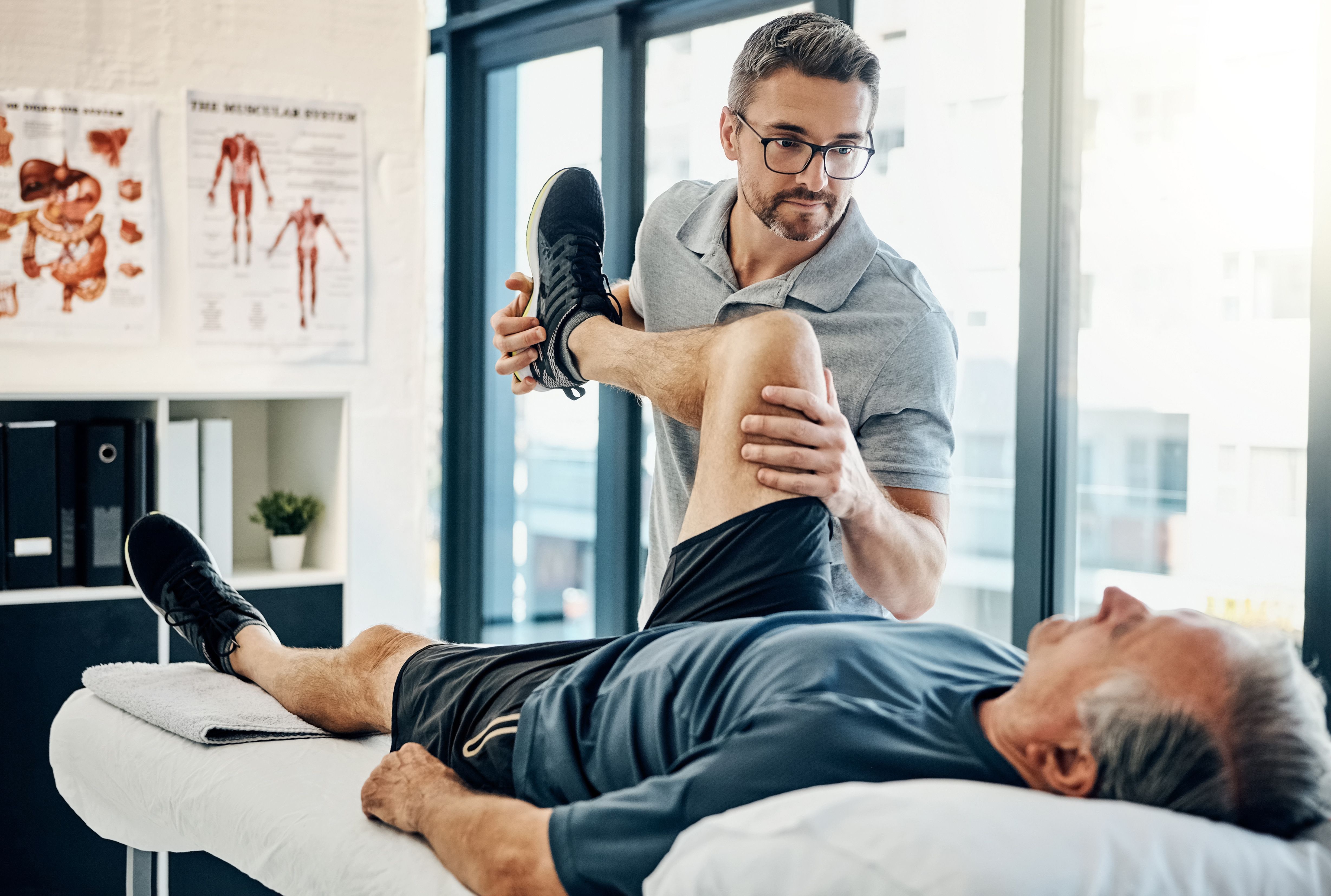 Physiotherapeut mobilisiert Bein eines Patienten auf der Behandlungsliege.